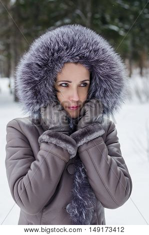 Beautiful pensive woman in winter jacket with fur hood walking in the woods