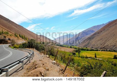 Long shot of the Elqui Valley with a street to the left and a blue sky with some white clouds in Chile, South America
