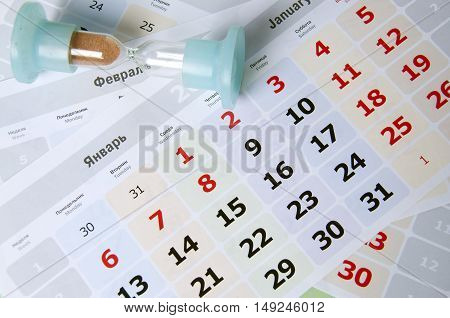 Still life of an hourglass lying on calendar sheets