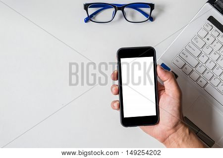 close up man hand holding smart phone wich eye glasses and laptop on while desk.Smartphone with blank screen and can be add your texts or others on smart phone.