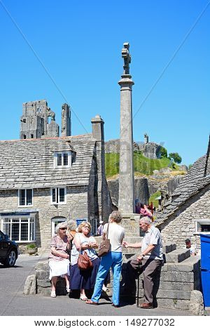 CORFE, UNITED KINGDOM - JULY 19, 2016 - Tourists around the stone cross in the village centre with the castle to the rear Corfe Dorset England UK Western Europe, July 19, 2016.