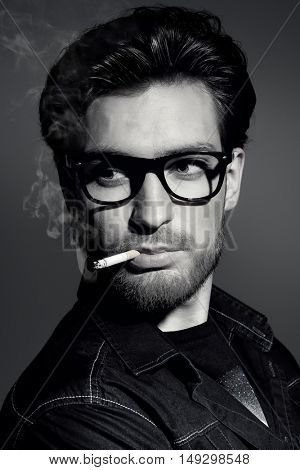 Black-and-white portrait of a smoking young man. Handsome young man thoughtfully and calmly smoking a cigarette. Men's beauty, fashion. 