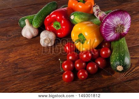 Heap of fresh organic tasty vegetables on brown wood background for menu or recipe. Healthy natural food on wooden table. Bright peppers and other cooking ingredients above view