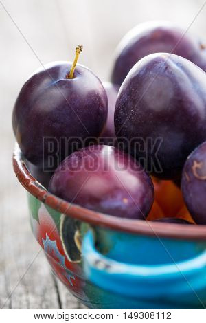 Fresh ripe plums in bowl on old wooden table.