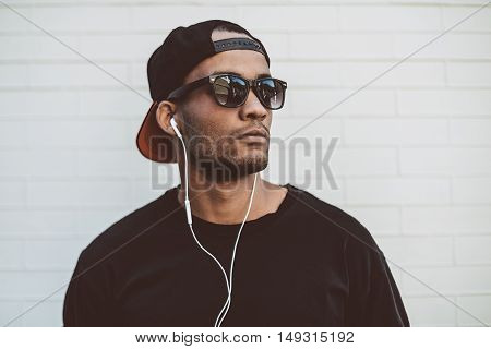 Music is his life. Handsome young African man in headphones looking away and looking serious while standing in front of the stoned wall outdoors