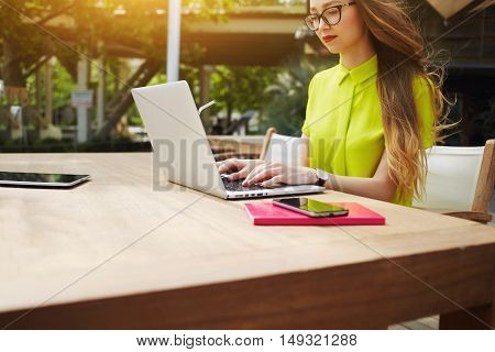Young woman manager is working on laptop computer while is sitting in cafe before interview with new employees. Pretty female student is keyboarding text message while studying via portable net-book