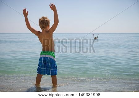 Happy boy in flippers standing on the ocean shore on a sunny day. Child going to swim in the sea. Vacations. Activities for child on the beach. Joy and happiness.