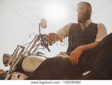 Serious Bearded Biker Man in black jacket sitting on motorbike outdoors