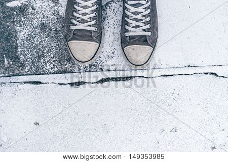 Young man standing on the street top view of worn gray sneakers on concrete floor with crack line as border - concept of obstacles difficulties hardship and restrictions in life.