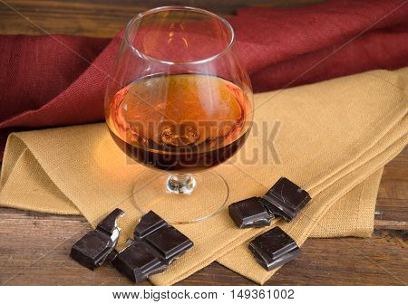 Glass of brandy and a chocolate on a old wooden table