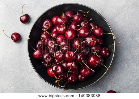 Fresh ripe black cherries in a black bowl on a grey stone background Top view.