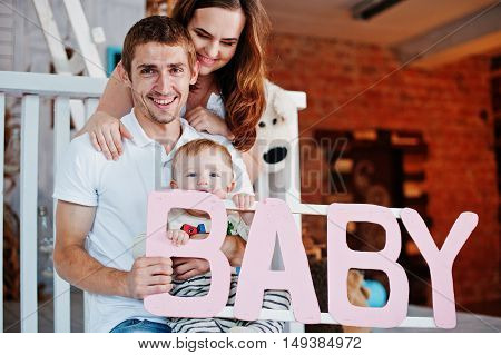 Young Caucasian Happy Family In Love Idoor Room With Letters Of The Word Baby