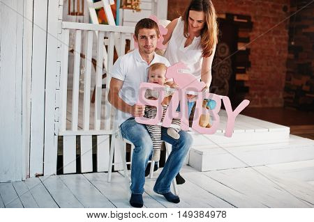 Young Caucasian Happy Family In Love Idoor Room With Letters Of The Word Baby