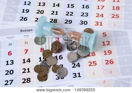 Hourglass on calendar sheets lie near the small coins