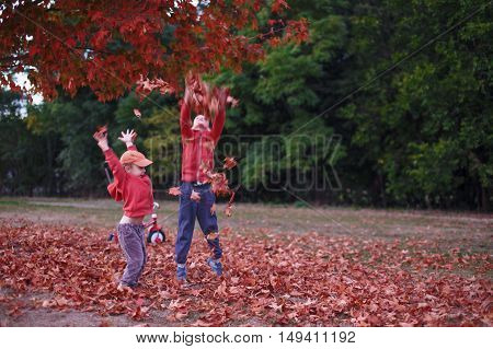 kids playing with fallen leaves. joyful boys frolic in the fallen maple leaves in the forest. the concept of happy autumn