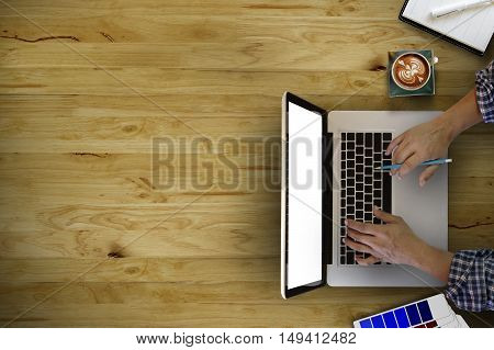 man's hands typing on a laptop with office suplies that is on a wooden desk .copy space. above view