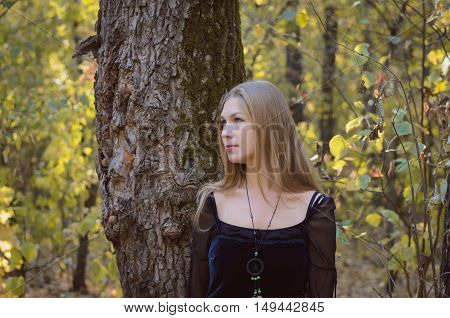 Blond Long-haired Girl In A Fantasy Black Dress In An Autumn Forest