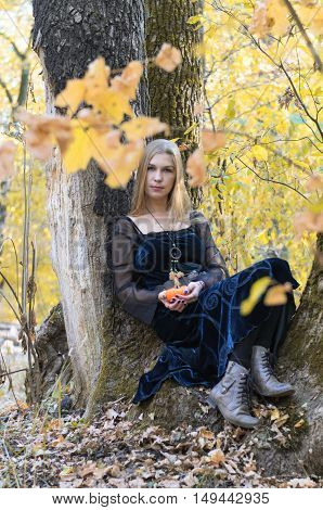 Portrait Of A Young Long-haired Blond Girl In A Black Dress Posing With A Pumpkin