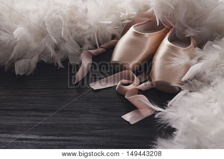 Pastel pink ballet shoes background. New pointe shoes with satin ribbon lay on black rustic shubby chic wood near feather boa, view with copy space