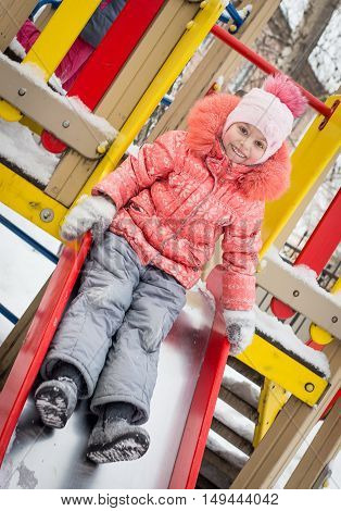 closeup portrait of happy laughing children in winter clothes playing on the bright colorful playground rolling downhill in the winter outside - Russia Moscow - February 25 2016