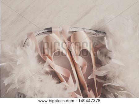 Pastel pink ballet shoes background. New pointe shoes with satin ribbon lay on white rustic shubby chic chair near feather boa, top view from above