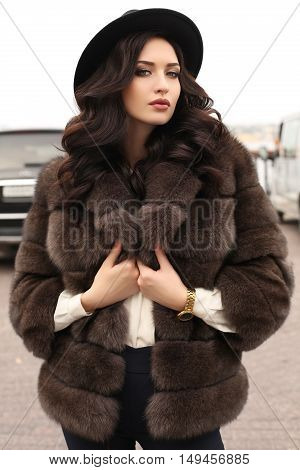 fashion outdoor photo of gorgeous woman with dark hair in elegant clothes and luxurious fur coat walking by autumn city