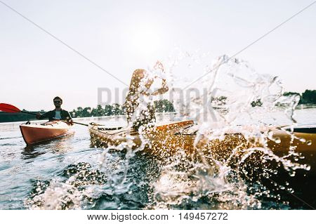 Enjoying summer day on the lake. Young couple kayaking on lake together and splashing water