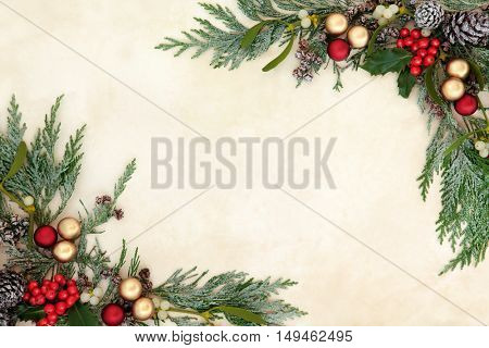 Christmas decorative background border with red and gold bauble decorations, holly, mistletoe and snow covered cedar cypress on old parchment paper.