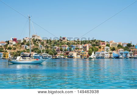 View over bay of Kastelorizo on sunny summer day. Island coast with typical colorful Greek houses, clear turquoise sea water and yacht. Dodecanese, Greece