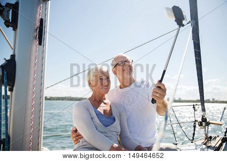 sailing, age, travel, technology and people concept - happy senior couple with smartphone selfie stick taking picture on sail boat or yacht deck floating in sea