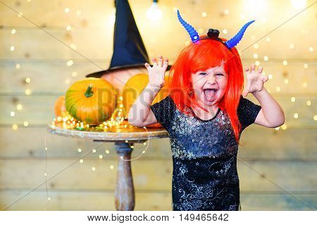 Happy deamon children during Halloween party playing around the table with pumpkins
