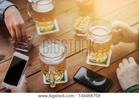 people, leisure, friendship and technology concept - close up of friends with smartphones and snacks drinking beer at bar or pub