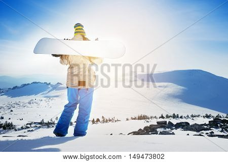 Girl snowboarder posing with snowboard on background of mountain