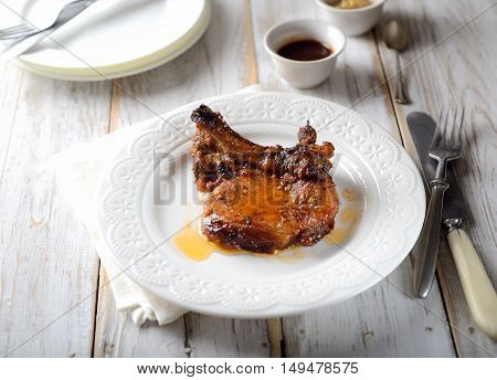 grilled steak on a white plate, sauce, vintage knife and fork on a wooden background