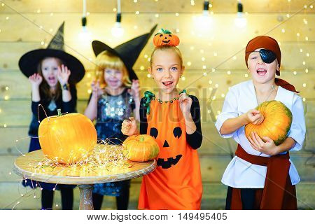 Happy group of witch children pirate and demons during Halloween party playing around the table with pumpkins