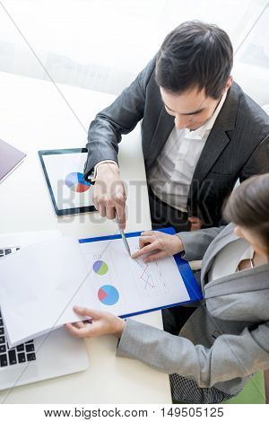 Two business partners analysing a financial report discussing the statistics and performance of their company high angle view showing the pie charts.
