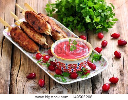 Homemade sauce dogberry with meat kebabs on wooden skewers.