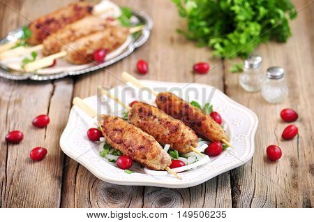 Homemade meat kebabs skewers with dogberry and onion salad on wooden background.