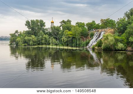 Summer landscape with artificial waterfall and Orthodox church on a Dnepr river island in center of Dnepr city Ukraine