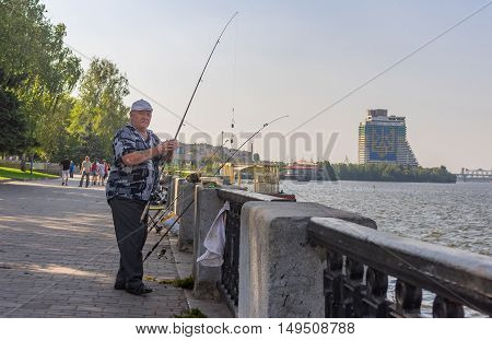 DNEPR, UKRAINE - AUGUST 21, 2016: Senior fisherman fishing on a Dnepr river embankment at summer weekend in Dnepr Ukraine at August 21 2016