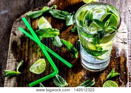 Glass of alcohol cocktail or lemonade. Mohito cocktail with lemon, lime, mint, ise cubes. Cold drink. Fresh lime and mint on wooden background