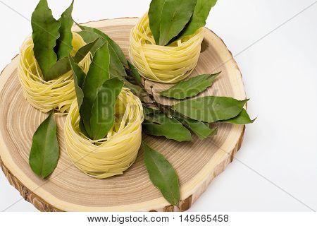 nests of pasta with bay leaves on a wooden cutting on white background