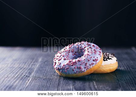 Close view at tasty donuts with blue and vanilla icing on a dark wooden background. With copy space. Toned for art effect