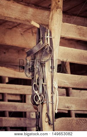 Various horse tack items hang in a stable.