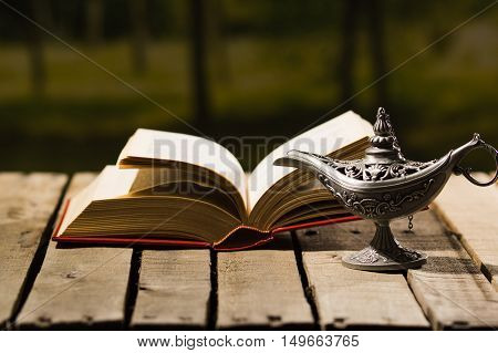 Thick book lying open on wooden surface, Aladin lamp sitting next to it, beautiful night light setting, magic concept shoot.