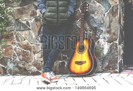 young man with a guitar while standing near the wall of stone