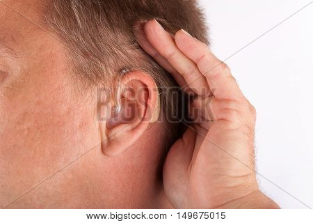 Ear of a man wearing hearing aid and cupping his hand behind his ear.