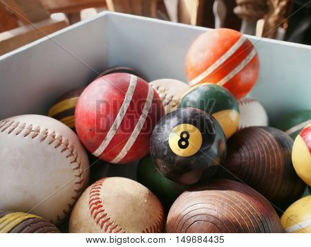 An old eightball in wooden bin full of vintage game balls including pool croquet and baseball.