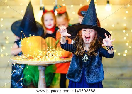Happy group of witch children pirate and demons during Halloween party playing around the table with pumpkins
