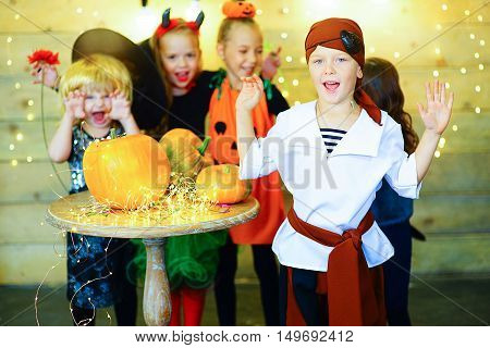 Happy group of witch children pirate and demons during Halloween party playing around the table with pumpkins